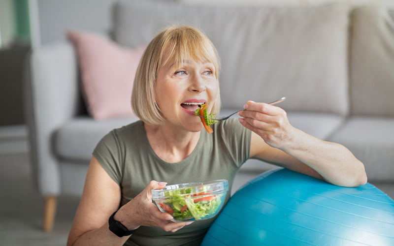 Senior woman eating healthy food against an exercise ball.