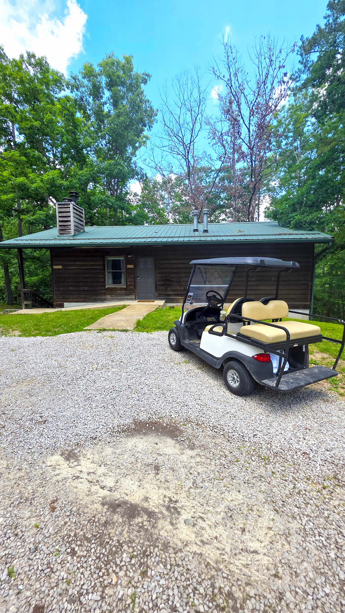 Trout Lodge Forest View Cabin Exterior Cabin Photo with lush green trees and a blue sky backdrop with Golf Cart parked in front of the cabin.