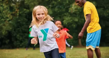 a ymca summer camp participant smiles as she plays outside at ymca summer day camp