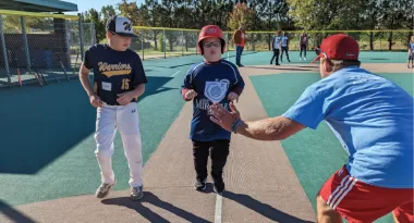 ymca adaptive sports volunteer coach high fives a miracle league player as they run to homebase