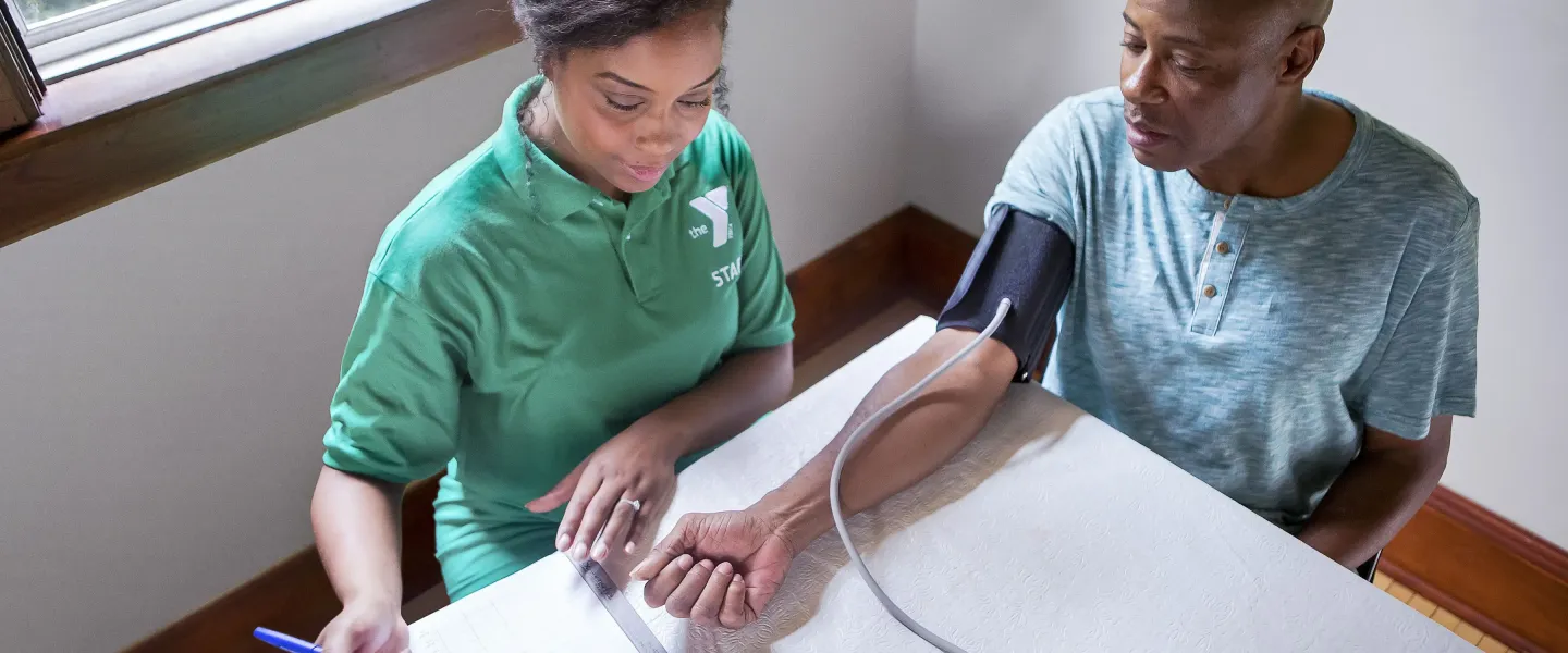 An African American YMCA staff member is captured taking an African American male's blood pressure.