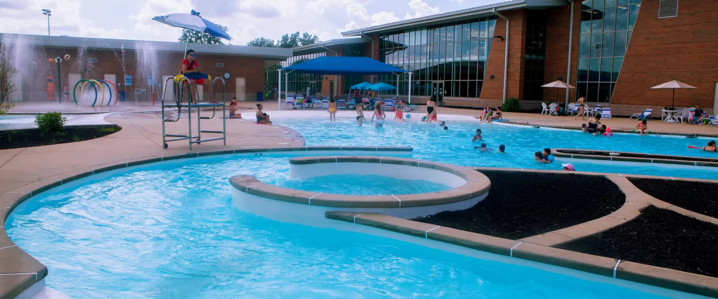 Carondelet Park Rec Complex Gym St. Louis, MO Outdoor Aquatic Center featuring a water slide, lazy river, zero-depth entry pool, kiddie splash pad and play structure, and lap pool.