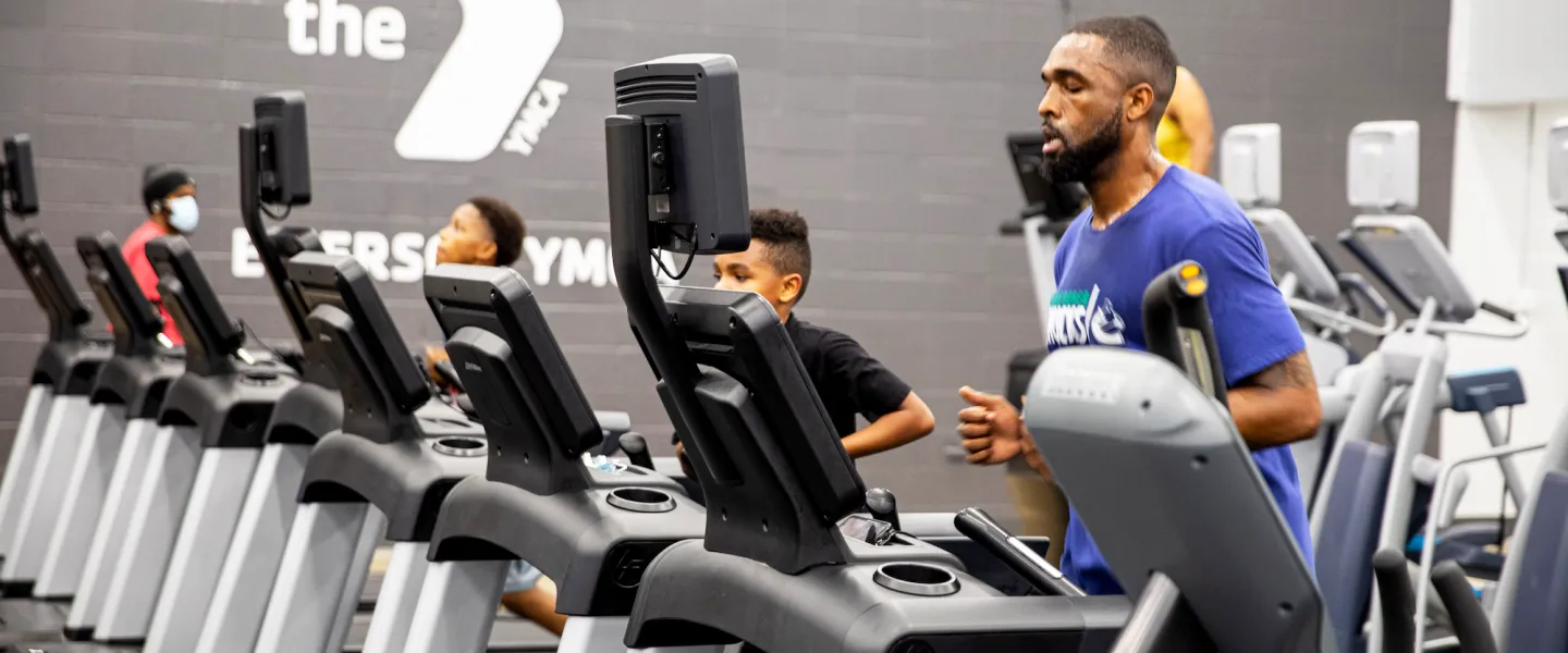 A dad and his two sons run on treadmills at a YMCA fitness center, staying active together during a family workout session.