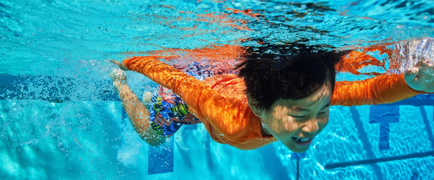 Child swimming underwater in a YMCA outdoor swimming pool with clear blue water.