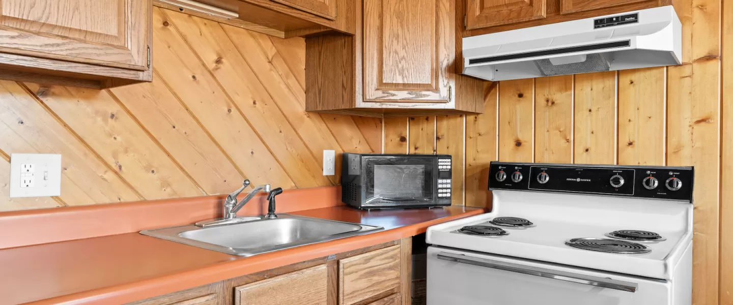 Compact kitchen area with microwave, stove, and refrigerator next to dining table in shared space