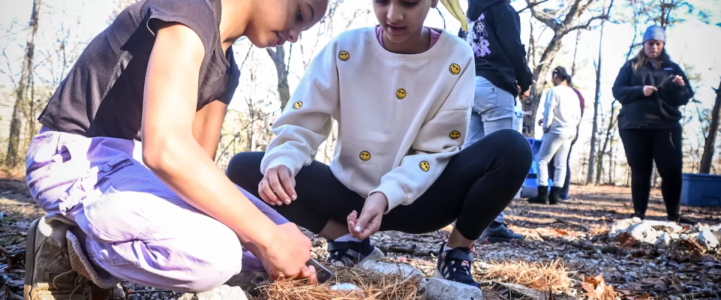Students working together to start a campfire with sticks and kindling