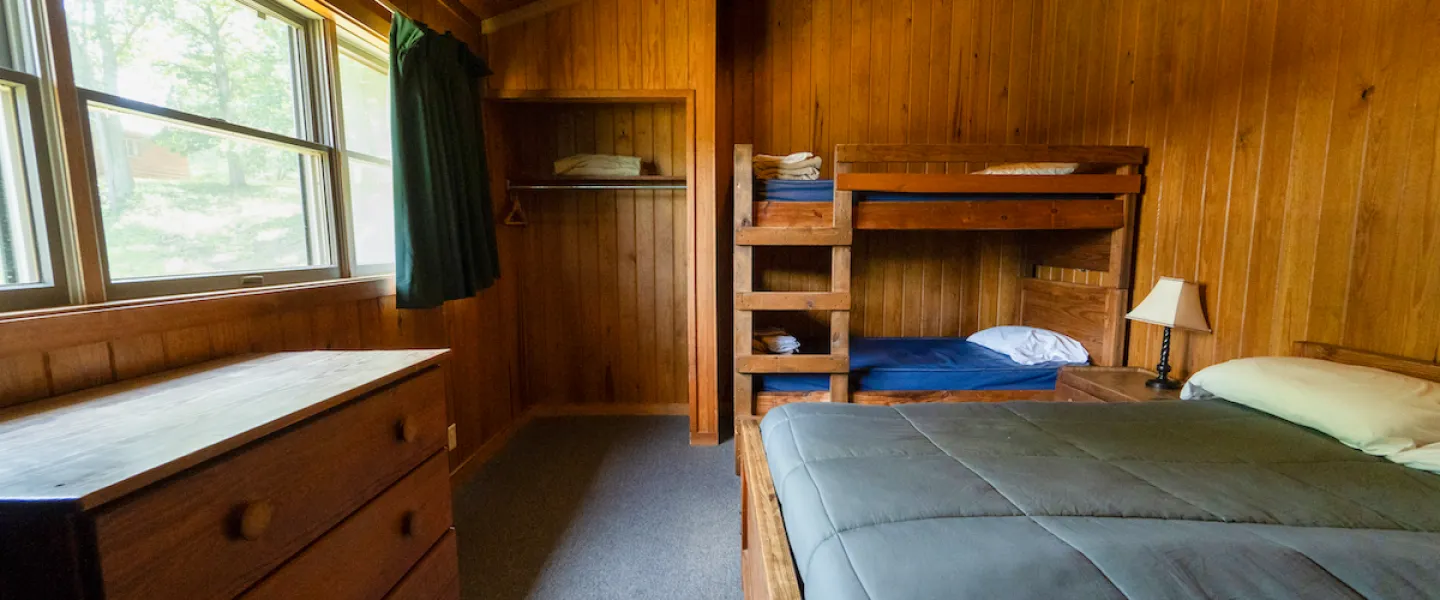 Guest room with a queen bed and two twin bunk-beds, with a dresser, closet, and linens in a Lake View Cabin at YMCA Trout Lodge