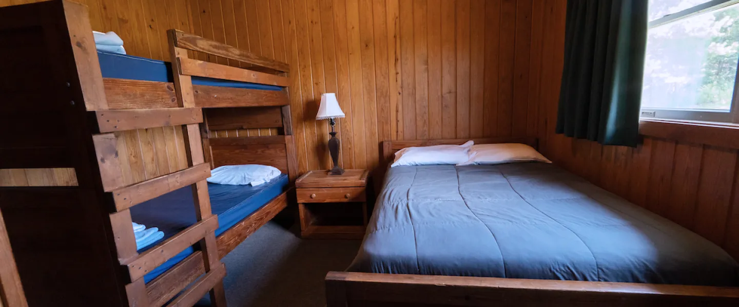 Guest room in a Lake View Cabin at Trout Lodge featuring a queen bed and two twin-size bunk beds with linens provided