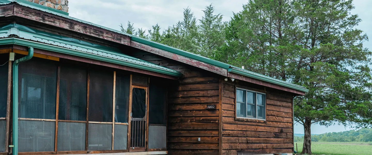Exterior photo of a Lake View Cabin at YMCA Trout Lodge showing a screened-in porch and chimney of the living room fireplace. 