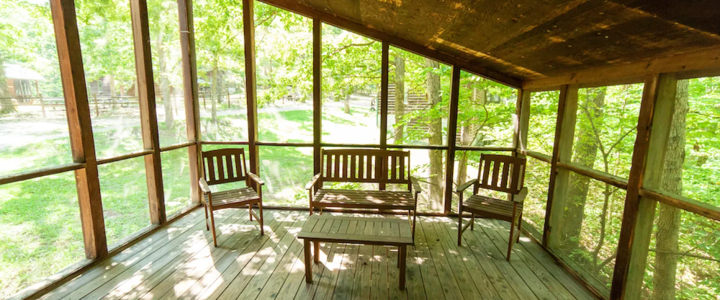 The wooden front porch and entrance to a rustic Forest View Cabin nestled among the trees at YMCA Trout Lodge.