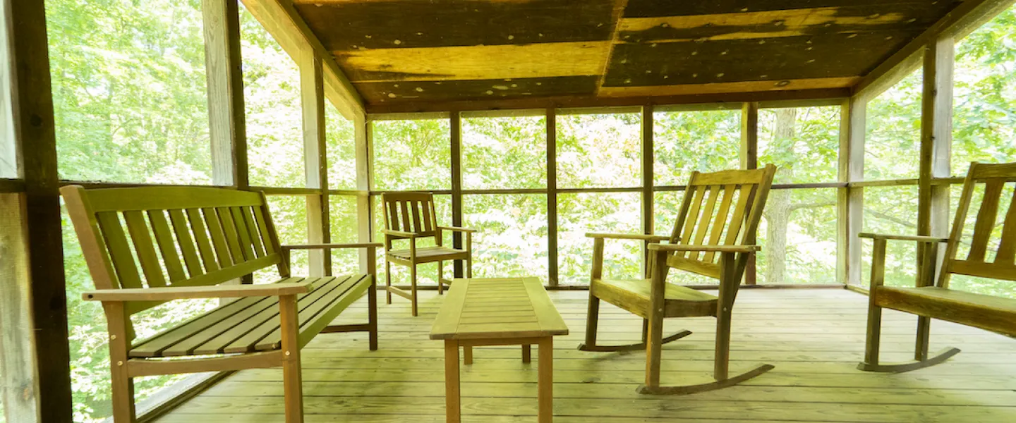 Two wooden rocking chairs on the screened-in porch of a rustic Forest View Cabin, looking out into the serene woods of YMCA Trout Lodge.