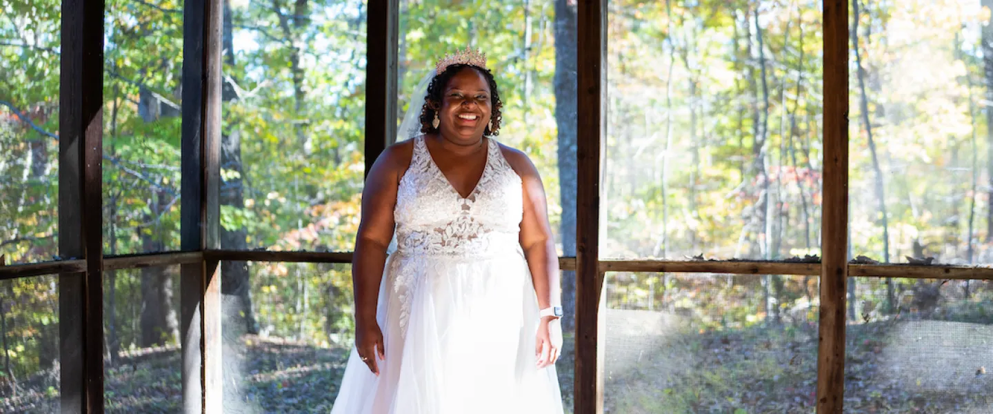 A smiling bride in her wedding dress posing on the rustic screened-in porch of a Trout Lodge cabin.