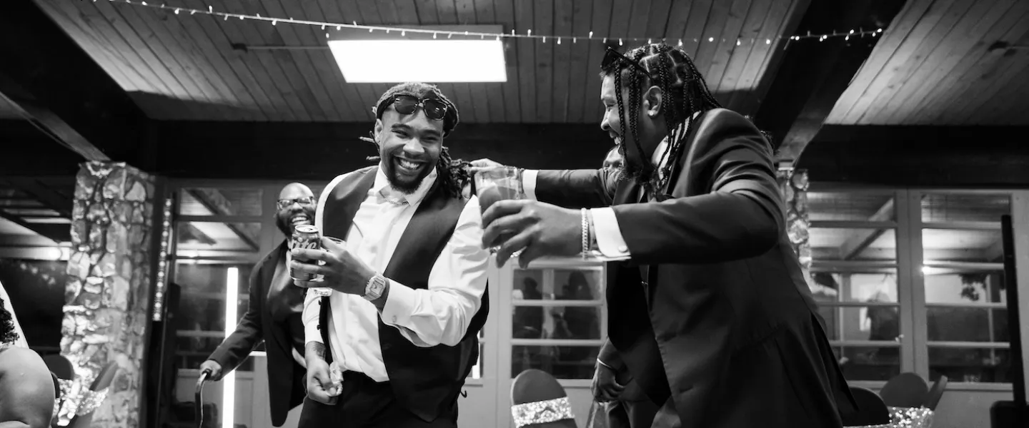 Two groomsmen laughing and dancing together during a lively wedding reception at YMCA Trout Lodge.
