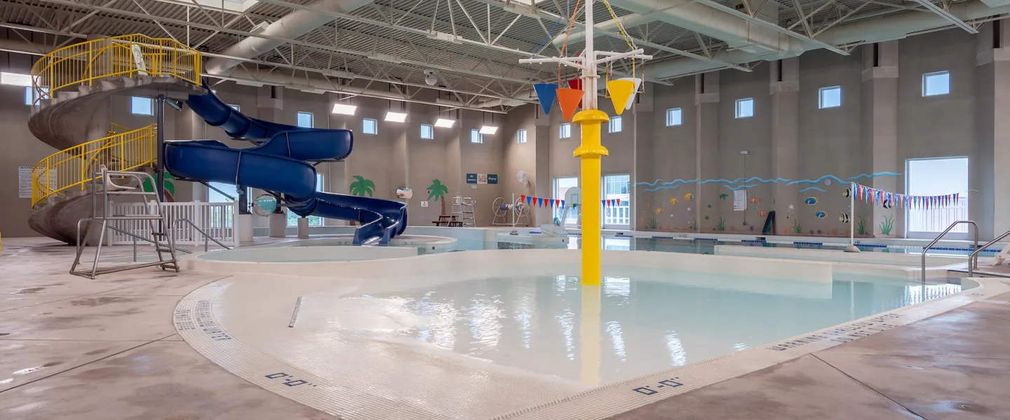 Ste. Genevieve County YMCA indoor swimming pool featuring a zero-depth entry kiddie splash pad, water slide, lazy river, whirlpool, and lap swimming lanes.