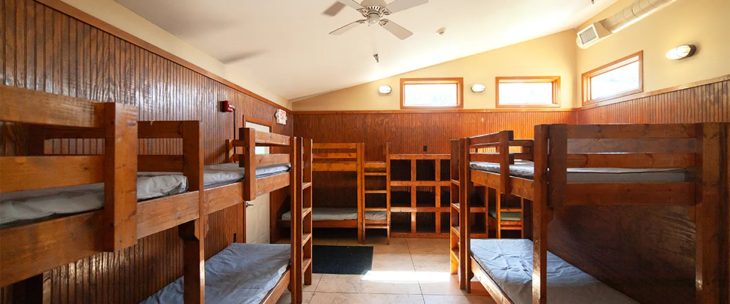 A well-lit Main Camp sleeping area with multiple sets of sturdy, wooden bunk beds.
