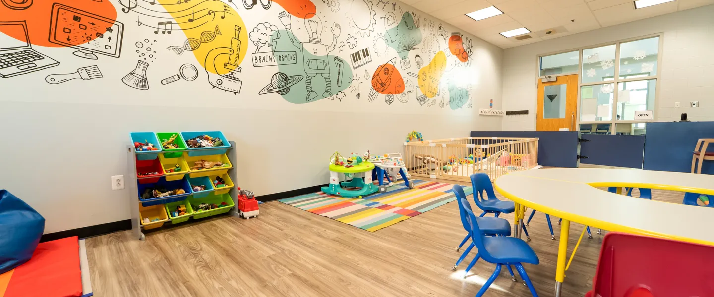 Close-up of a vibrant wall mural in the RiverChase Y Child Watch room featuring whimsical illustrations of robots and atoms next to a toy storage unit and blue seating.