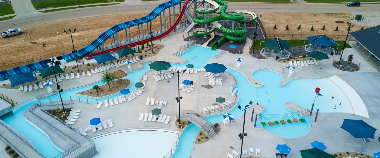 An angled aerial perspective of the Ste. Genevieve YMCA outdoor waterpark, highlighting the large twisting green slides and the expansive main swimming pool.