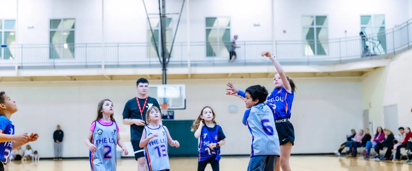 A young girl shoots a basketball attempting to score in a YMCA Youth Basketball game.