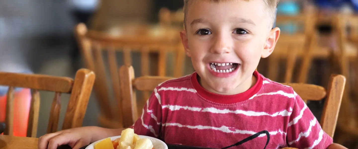 A young boy smiles next to a plate of breakfast food and a bowl of Fruit Loop cereal in the Trout Lodge Dining Hall