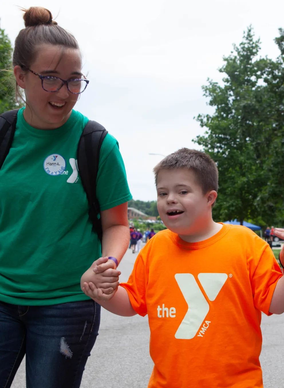 Two camp counselors holding hands with child as they walk down the street