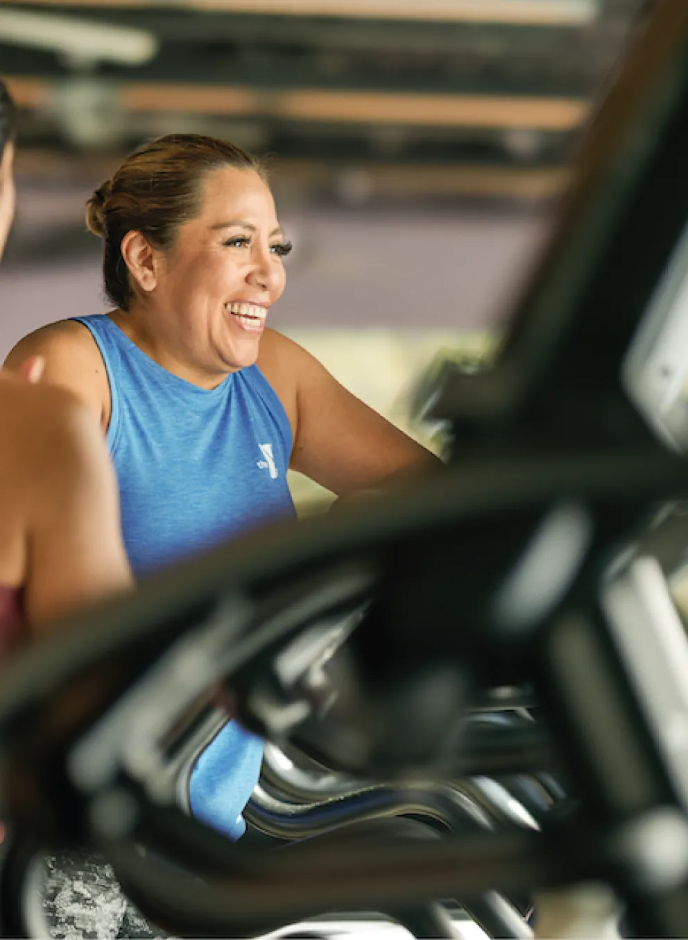 Two females talking and smiling as they work out on elliptical cardio machines in a YMCA Fitness Center.