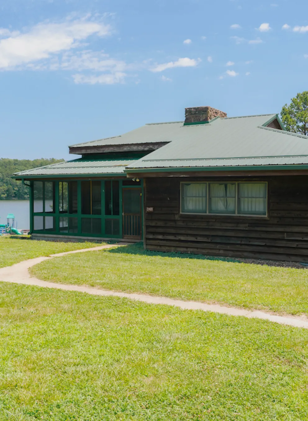 Exterior photo of a Lake View Cabin at YMCA Trout Lodge showing the screened-in porch, views of Sunnen Lake, and a nearby playground for families and kids
