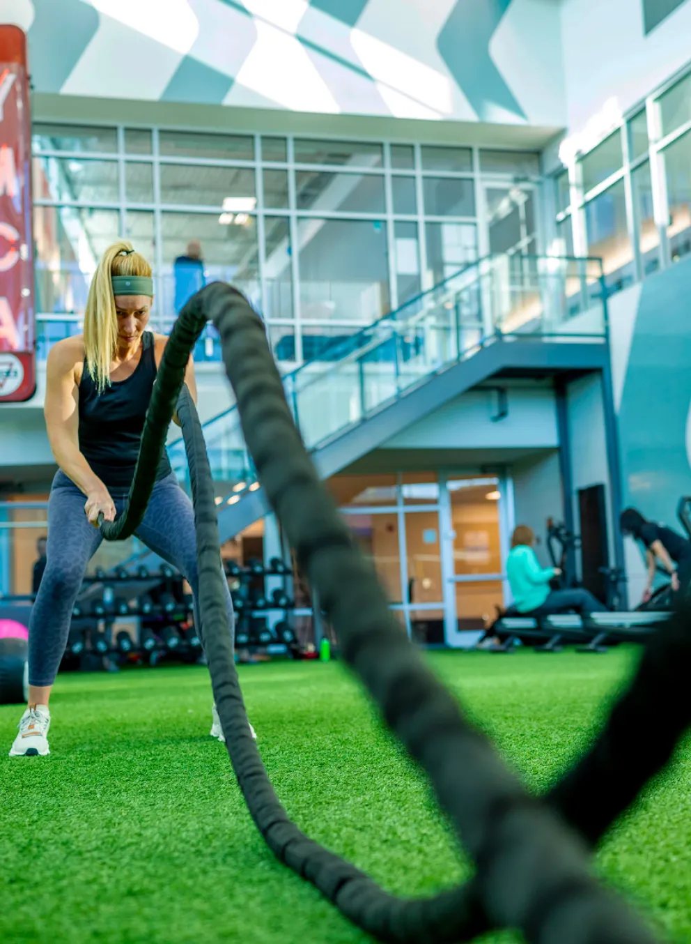 A woman has a focused and determined look on her face as she uses workout battle ropes during a small group training Functional Fitness group exercise class at a St. Louis Missouri YMCA.