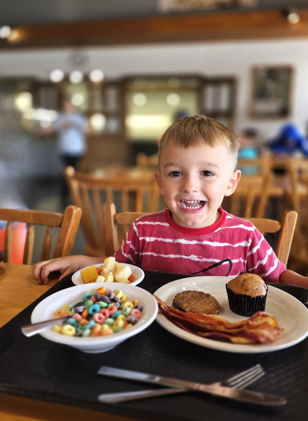 A young boy smiles next to a plate of breakfast food and a bowl of Fruit Loop cereal in the Trout Lodge Dining Hall