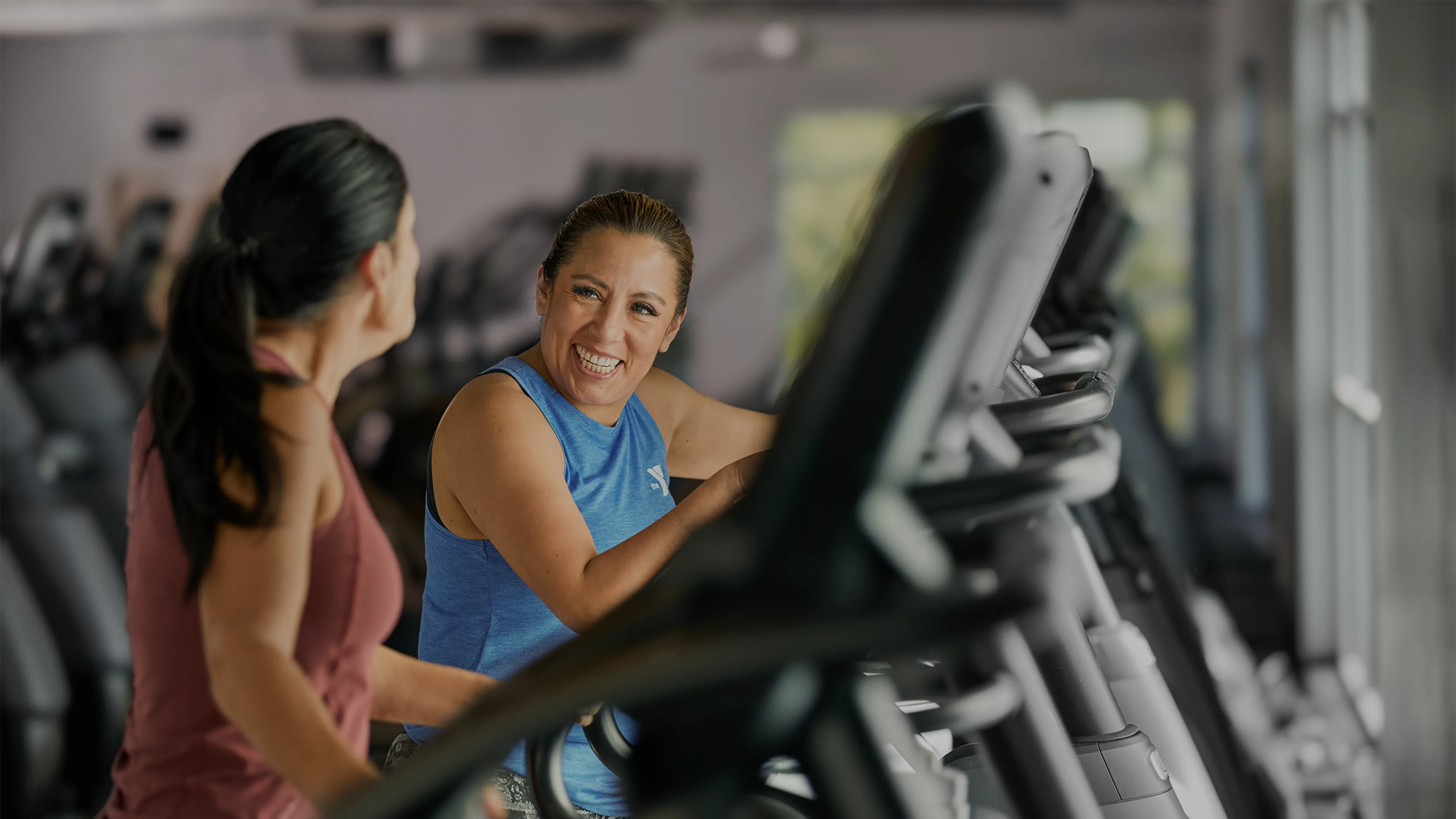 Two Women Laugh as they Workout in a YMCA Fitness Center