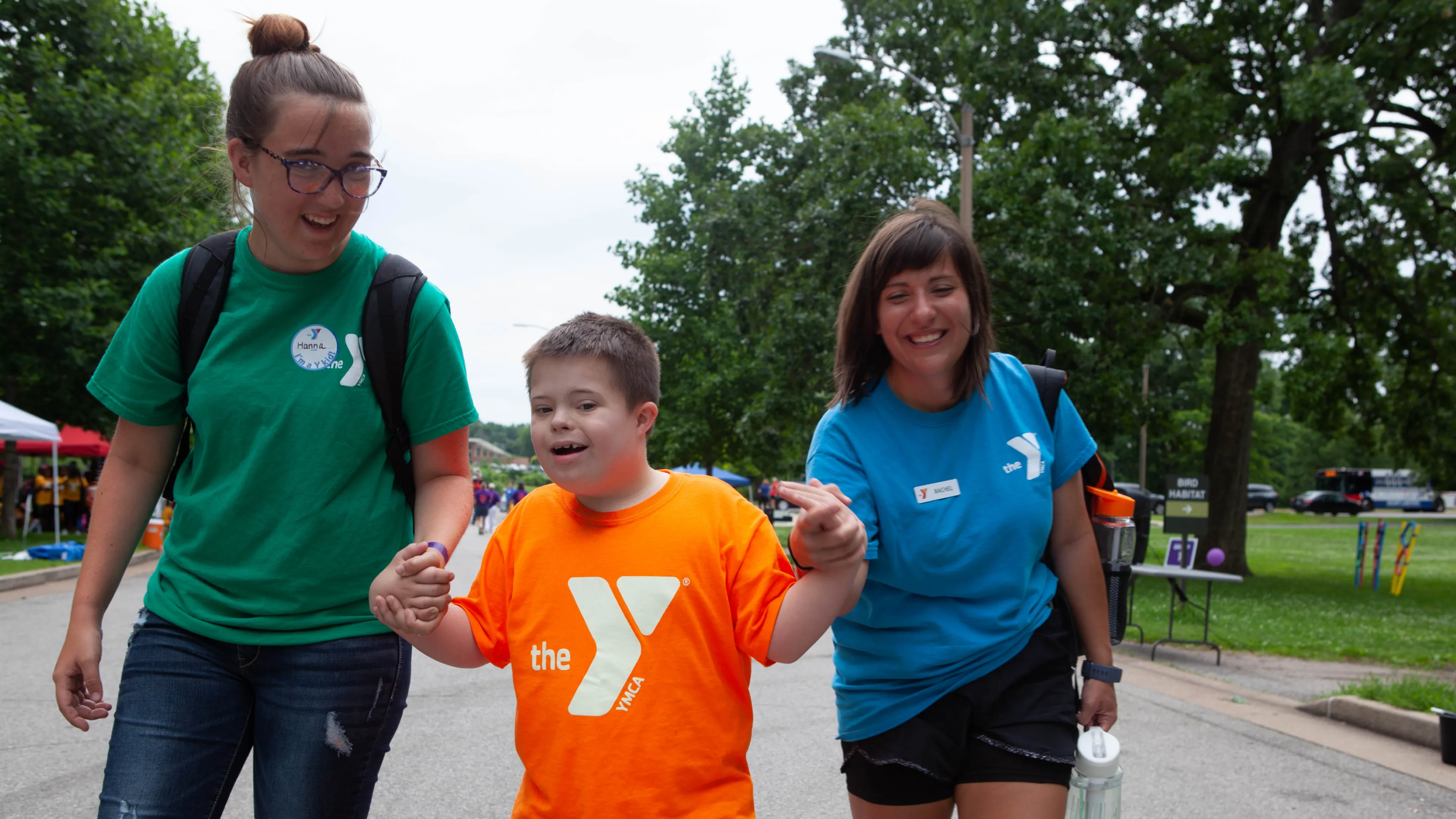 Two camp counselors holding hands with child as they walk down the street