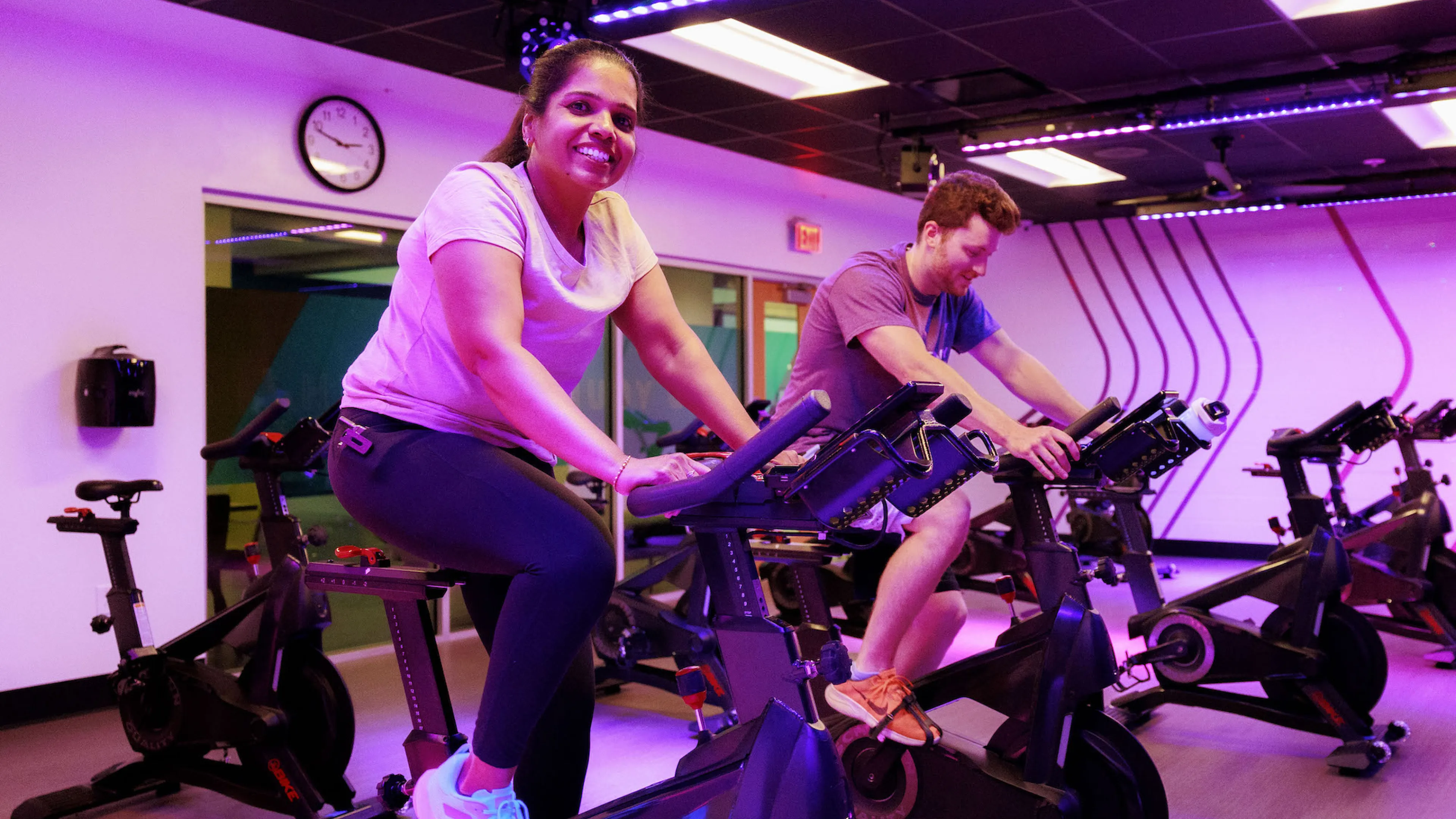 A woman smiling at the camera while exercising on a spinning bike inside of the Chesterfield YMCA's cycling studio during a group exercise class