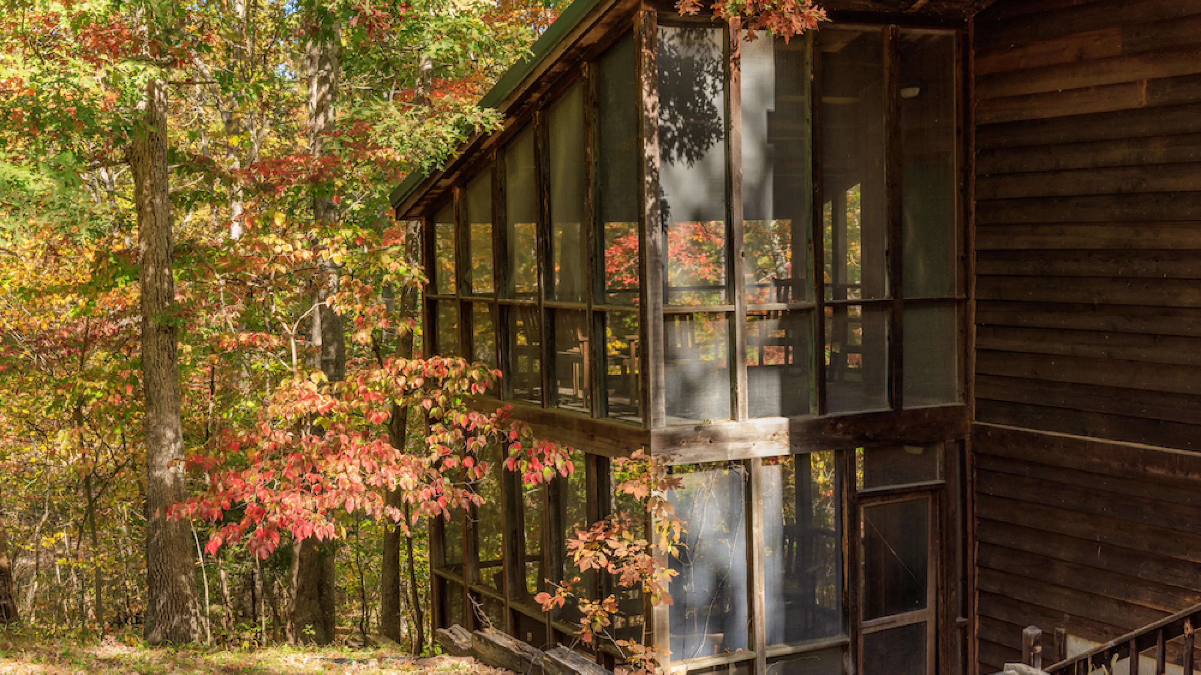 A view of the two-story screened porches in a Forest View Cabin at YMCA Trout Lodge surrounded by orange colored fall leaves on the forest trees