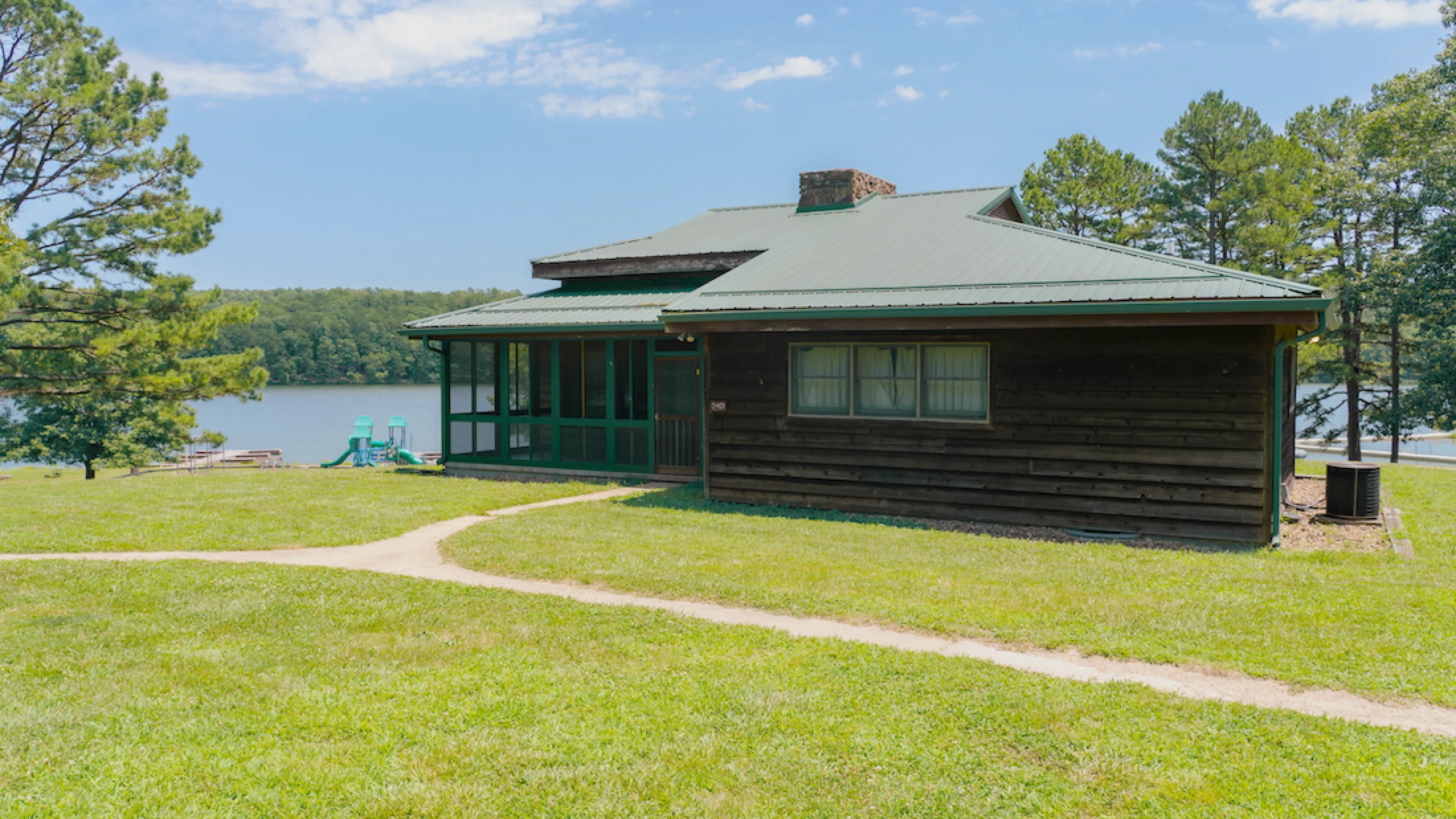 Exterior photo of a Lake View Cabin at YMCA Trout Lodge showing the screened-in porch, views of Sunnen Lake, and a nearby playground for families and kids