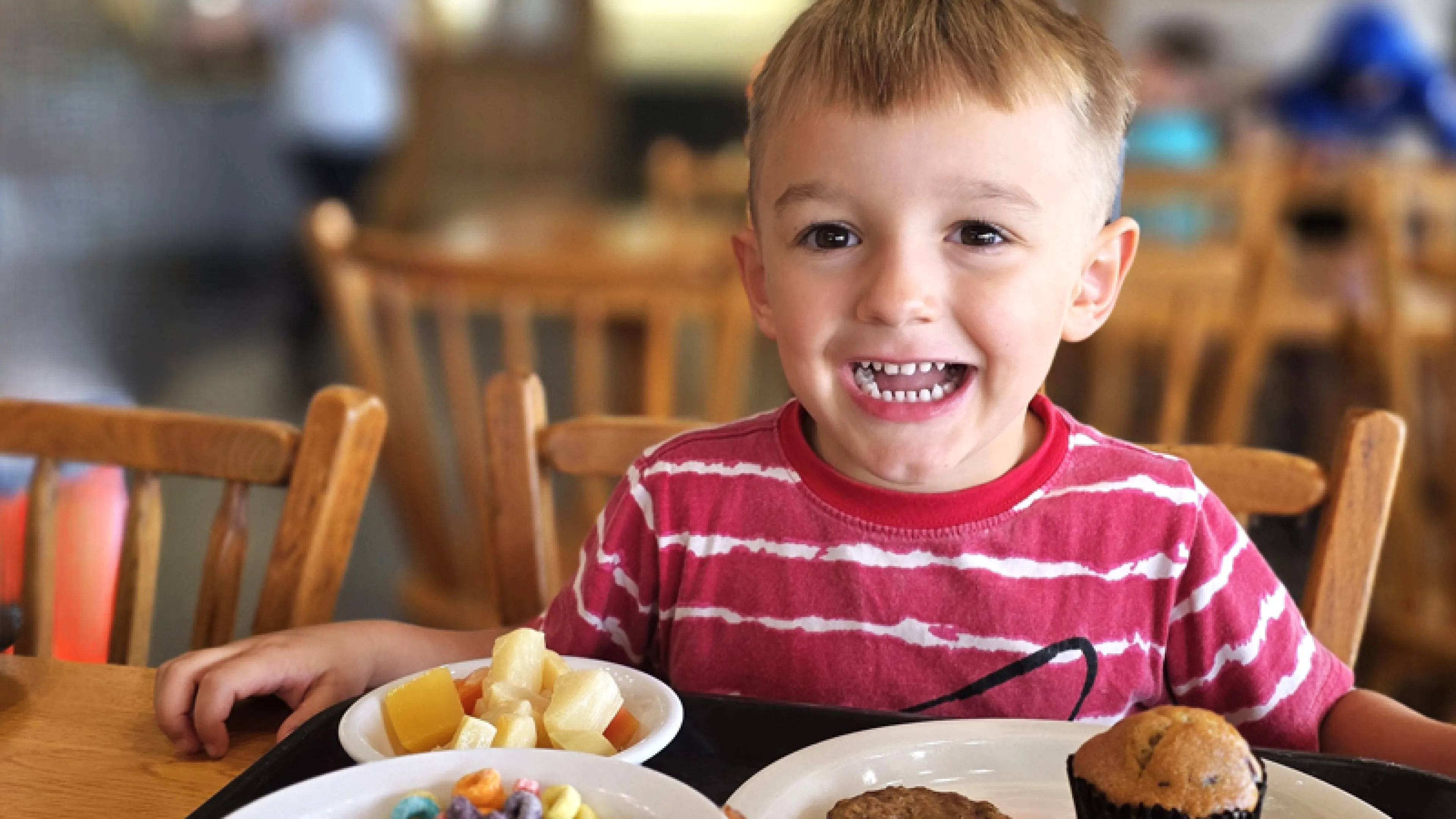 A young boy smiles next to a plate of breakfast food and a bowl of Fruit Loop cereal in the Trout Lodge Dining Hall
