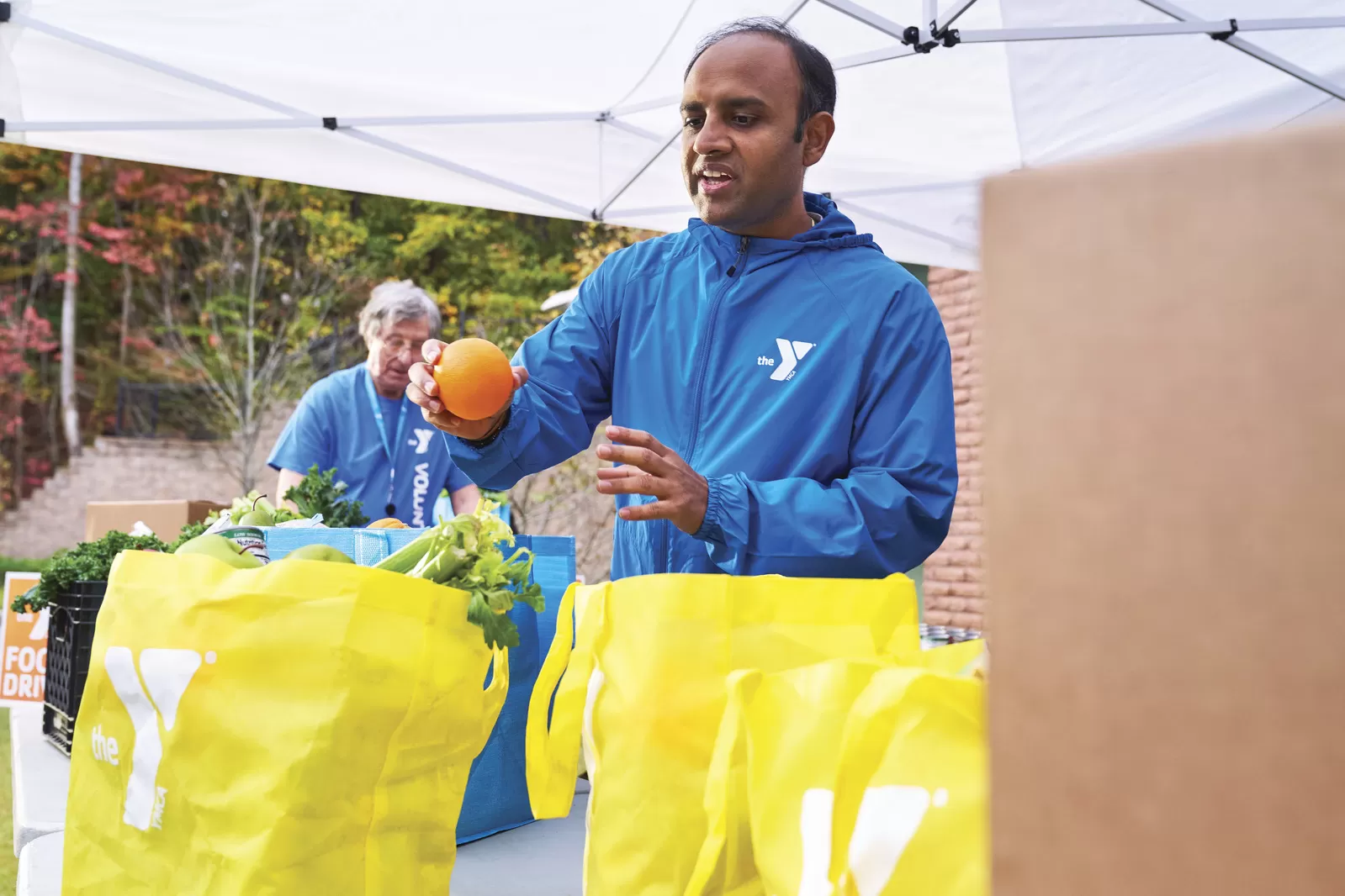 A man places an orange into a ymca grocery bag.