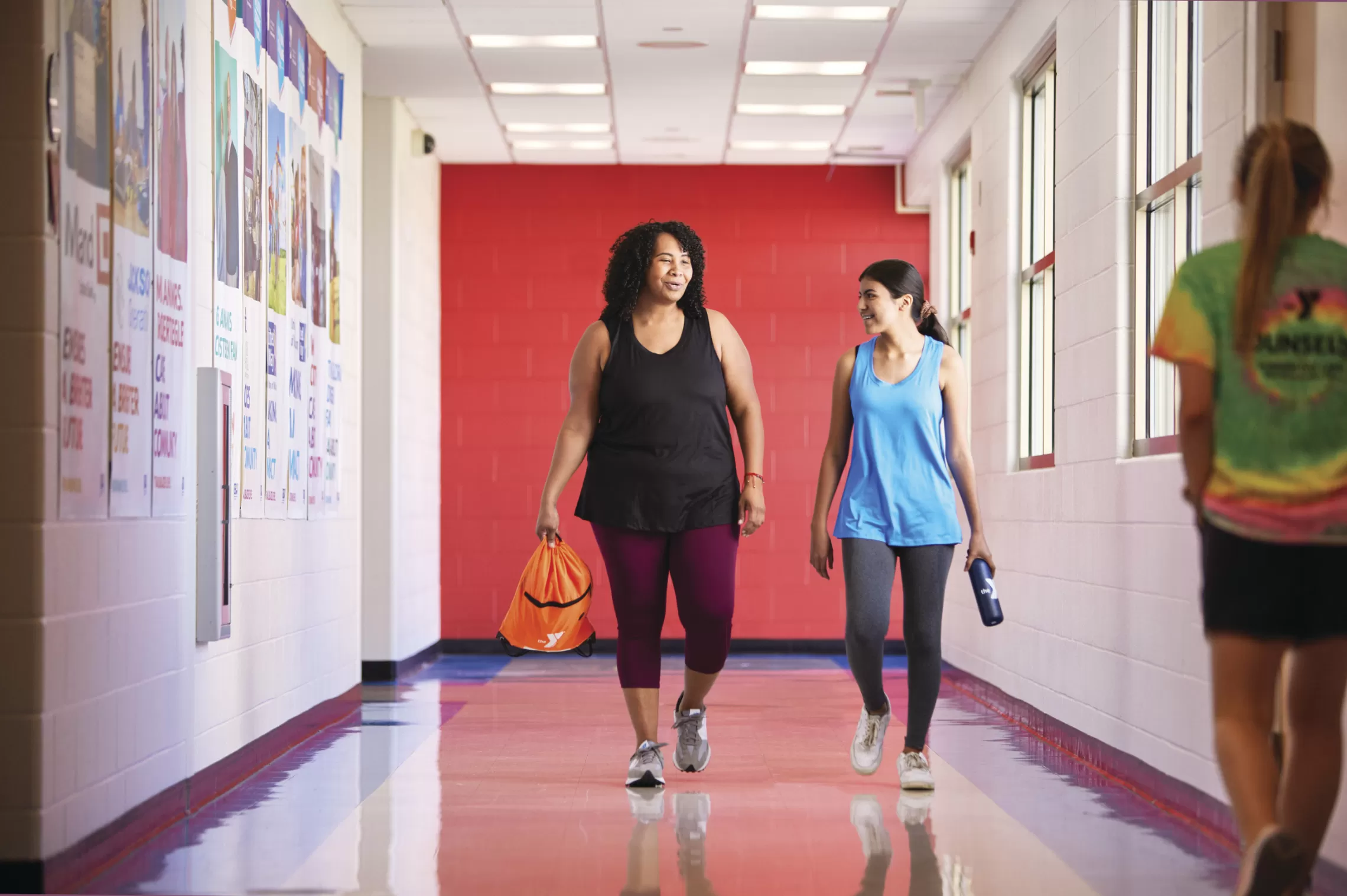 Two women walk down the hall of a ymca talking