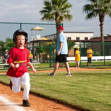 A young boy in a Cardinals jersey plays baseball on Miracle league field.