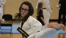 Thumbnail: An image of a teenage Caucasian female participant in the YMCA karate program. She is captured kicking toward her instructor, and is dressed in a white karate uniform with black accents.