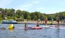 Thumbnail: A group of male and female teens enjoy the lake and water-based activities during a program at Trout Lodge YMCA. The students are doing a variety of activities like kayaking, paddle-boarding, and swimming in inflatable floaties. All teenagers look to be having a fun experience.