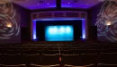 Thumbnail: Theater with rows of seating facing stage. Stage lit with side lights. Dim theater lighting throughout room.