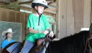 Thumbnail: Ranch staff with younger camper on horseback