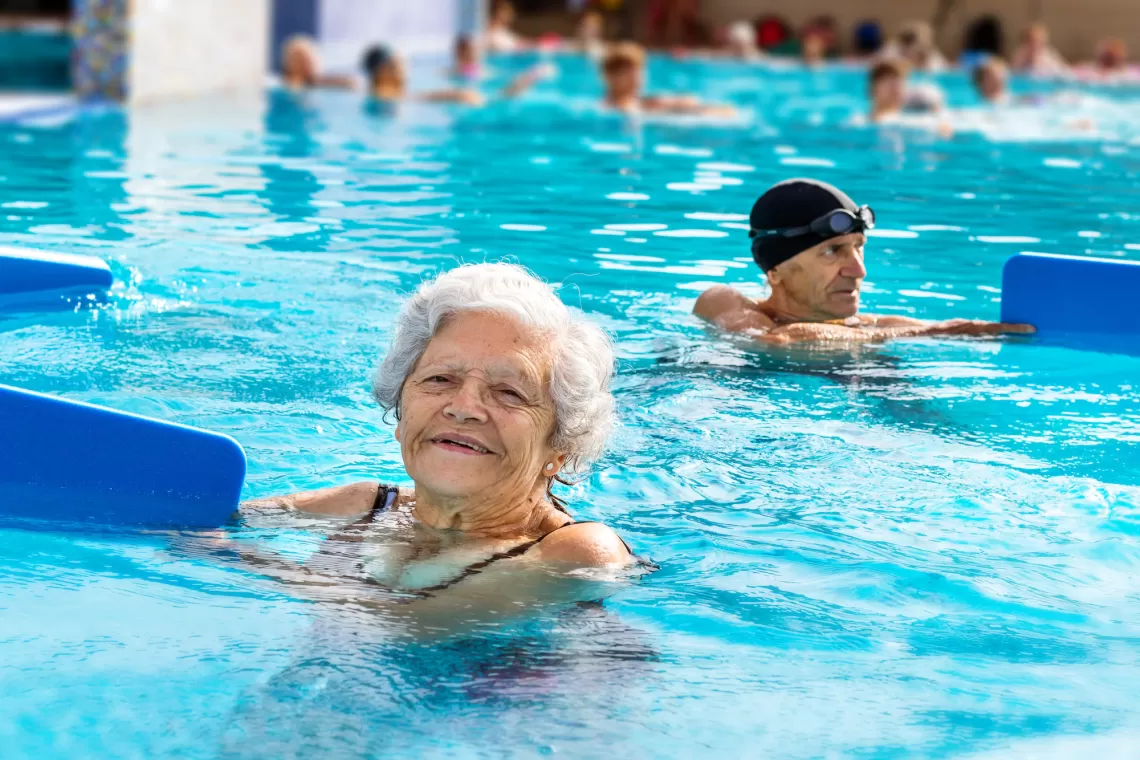 YMCA water fitness class and water aerobics participant with a kick-board in a YMCA outdoor swimming pool.