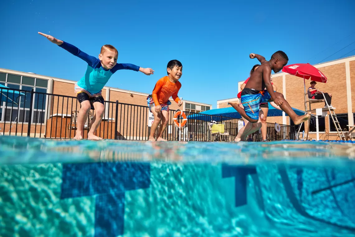 YMCA outdoor swimming pool with children jumping into the pool supervised by a YMCA Lifeguard