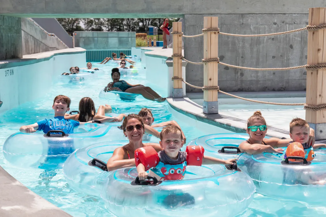 Guests relaxing in inner tubes while floating down the winding lazy river under a sunny sky at the Ste. Genevieve YMCA River Rapids Waterpark.
