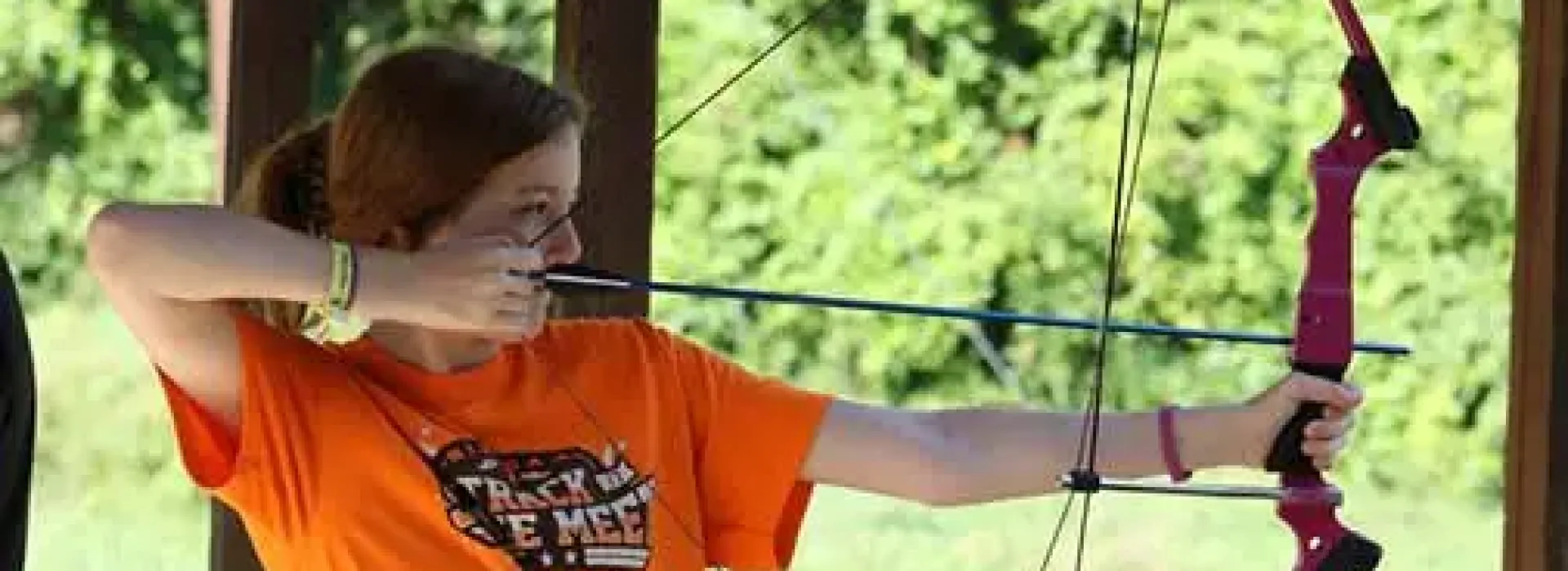 girl pulls back a bow and arrow and aims, preparing to shoot a target