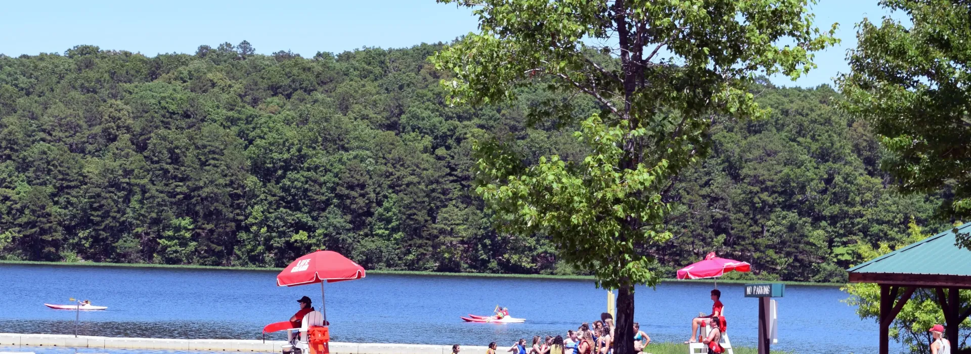 An image of a waterfront that is booming with swimmers, lifeguards and boats on the lake. It was taken on a sunny summer day.
