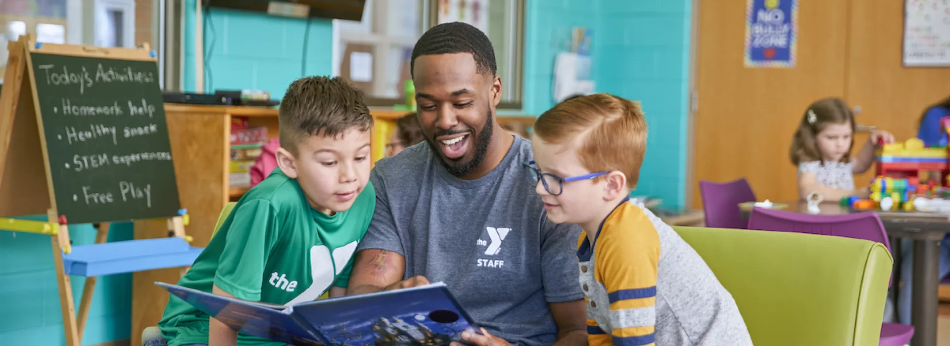 ymca y club staff reading a book to two boys in the ymca y club before and after school program