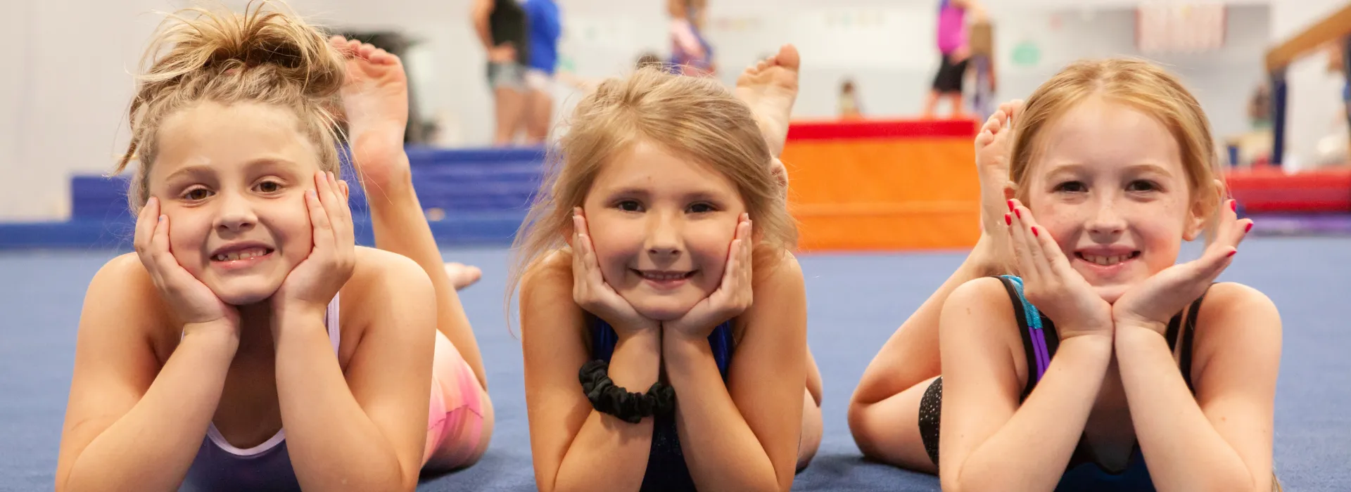 three girls pose and smile in a ymca gymnastics class