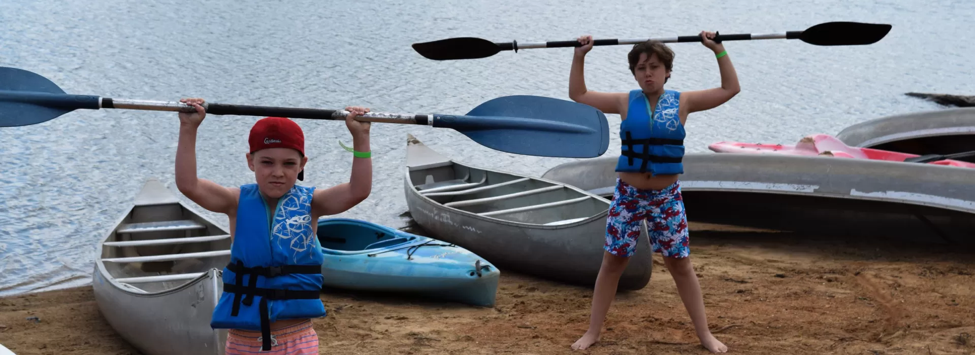 Young boys holding kayak paddles above their heads
